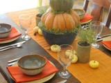 a fall-Thanksgiving centerpiece of stacked pumpkins in a pot, some greenery and mini pumpkins