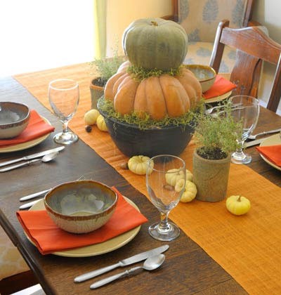 a fall Thanksgiving centerpiece of stacked pumpkins in a pot, some greenery and mini pumpkins