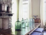 a farmhouse space with large green glass bottles that line up the table and add a vintage feel to the space